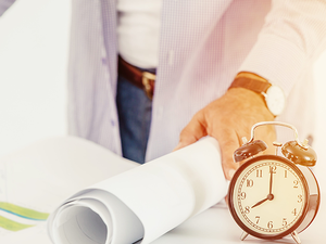 Ein Mensch steht am Tisch und rollt eine Planungskarte auf. Davor steht eine Uhr.